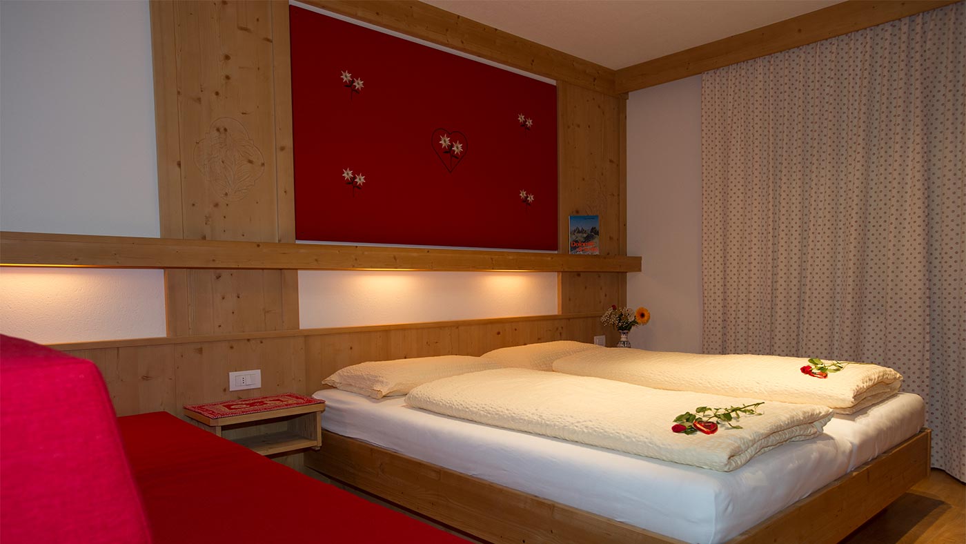 Il romantico letto di una camera matrimoniale in legno nel Residence Edelweiss - due rose rosse sul letto