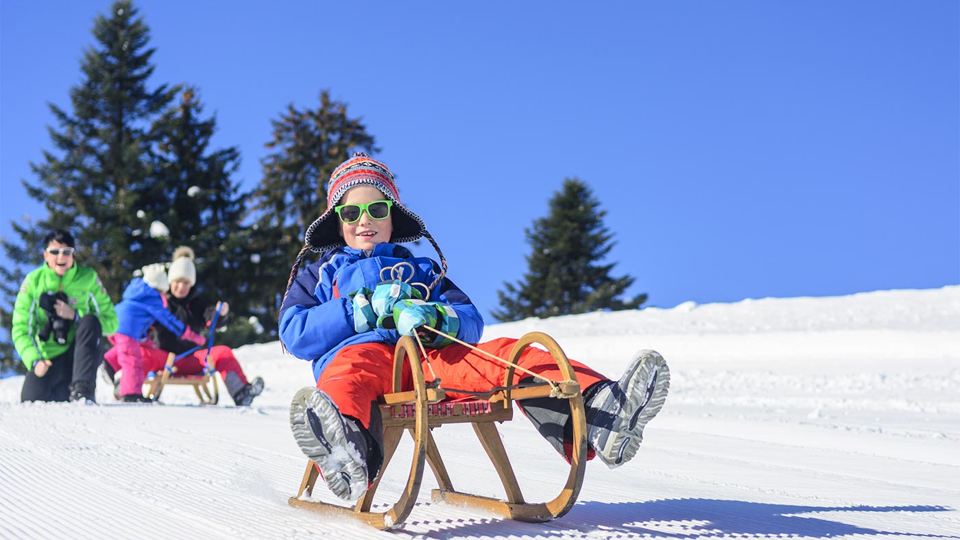 Sledge slope in San Candido, in the foreground - a child sits with sunglasses on his sledge